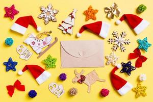 Top view of craft envelope with Christmas decorations and Santa hats on yellow background. Happy holiday concept photo