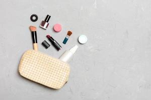 vista superior de los productos de maquillaje caídos de la bolsa de cosméticos sobre fondo de cemento. concepto cosmético con espacio para tu diseño foto