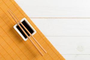 Bamboo mat and soy sauce with sushi chopsticks on white wooden table. Top view with copy space background for sushi. Flat lay photo