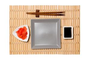 Empty gray square plate with chopsticks for sushi, ginger and soy sauce on yellow bamboo mat background. Top view with copy space for you design photo