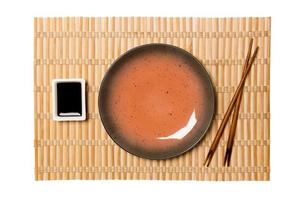 Empty round brown plate with chopsticks for sushi and soy sauce on yellow bamboo mat background. Top view with copy space for you design photo