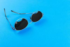 Black pinhole glasses on blue background. Medical concept. Top view photo