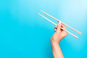 Wooden chopsticks holded with female hands on blue background. Ready for eating concepts with empty space photo