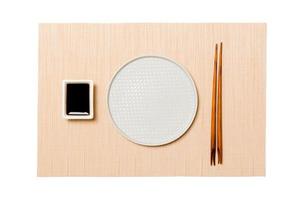 Empty round white plate with chopsticks for sushi and soy sauce on brown sushi mat background. Top view with copy space for you design photo