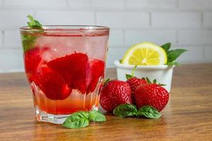 una bebida refrescante de verano con hielo, fresas y limón sobre un fondo de madera. el concepto de bebida de frutas. foto