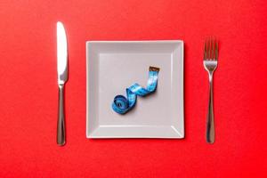 Measuring tape in a plate with fork and knife on both sides on red background. Top view of weight loss concept photo