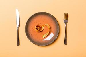 Round plate with measure tape inside with fork and knife on orange background. Top view of obesity concept photo