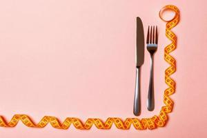Top view of fork and knife and curled measuring tape on pink background. Diet concept with copy space photo