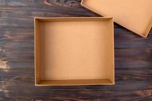 Opened brown blank cardboard box on wooden dark background, top view photo