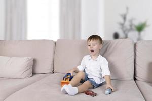 A handsome boy with joyful emotions on his face plays with toys in the room on the sofa. Educational games with children. photo