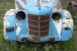 Vintage rusty blue car on the street with green grass. photo