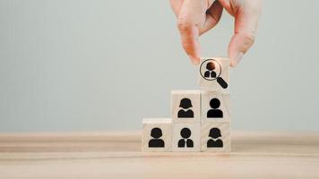 Hand hold wood cubes with magnifying glass focuses on the best employee icon to be a team leader for recruitment managers, and target customer concepts. HRM or Human Resource Management. photo