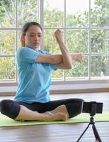 Young asian woman concentrate stretching follow online tutorial from smartphone before doing or practicing yoga at home. Young people domestic life concept. Selective focus. photo