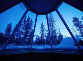 Room with outside window view of frosty Snow covering pine forest trees in twilight, skylight windows, snow view, winter time photo