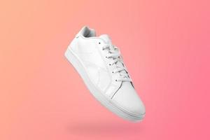 High angle view of white sneaker isolated on peachy background. Sportive pair of shoes for mockup. Fashionable stylish sports casual shoes. photo