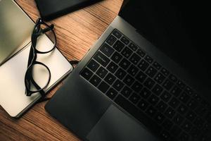 Top view of wood vintage desk focused on laptop with notepad, smartphone and glasses. Workplace. Work from home. Office desk. photo