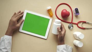 un médecin tient un contenant de médicaments tout en utilisant une tablette video