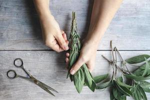 Sage smudge stick making, hands wrap string around sage leaf bundle, natural incense for home and meditation photo