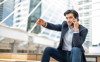 Closeup of young caucasian serious man using modern smartphone device while sitting and pointing to his friend at the public area. photo