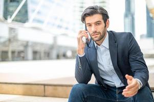 Closeup of young caucasian serious man using modern smartphone device while sitting at the public area. photo