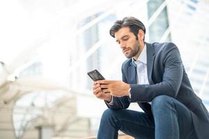 Closeup of young caucasian serious man using modern smartphone device while sitting at the public area, while looking at the social network on smartphone. photo