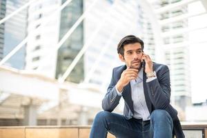 Closeup of young caucasian serious man using modern smartphone device while sitting at the public area. photo