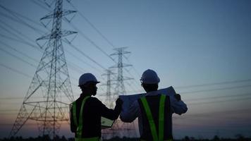 Two electrical engineers discussing a project on a high-voltage tower in the evening. video