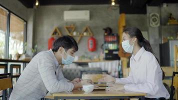 A man and a woman, an Asian businessman, wearing a white shirt. Sitting holding a tablet to talk about a project In a coffee shop video