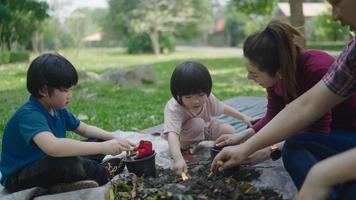 une famille de deux fils aide à ramasser des restes de fruits et légumes pour apprendre à faire du compost naturel. dans le jardin de devant pendant les vacances video