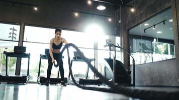 atleta asiática desportiva mulheres exercitam treino com corda de batalha no ginásio cross fitness. video