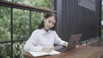 une femme d'affaires asiatique assise devant un ordinateur portable dans son jardin. video