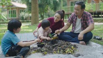Eine Familie mit zwei Söhnen hilft beim Austragen von Obst- und Gemüseresten, um zu lernen, wie man natürlichen Kompost herstellt. im Vorgarten an Feiertagen video