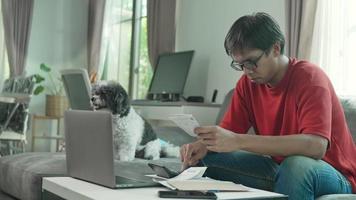 Man looks at laptop use app, comparing data, check receipts and invoices sit in living room, working from home office. Accounting job, personal finances management, prepare financial report concept video