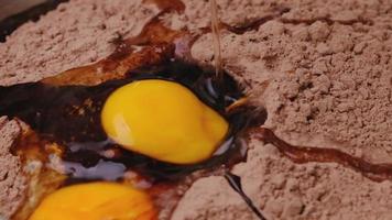 el huevo de gallina cae en cámara lenta en el primer plano de la harina de cacao. receta paso a paso para hacer galletas de chocolate caseras o bizcocho de brownies. video