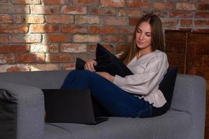 mujer en un sofá sosteniendo una almohada y mirando una laptop foto