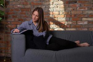 mujer acostada en el sofá y escribiendo en un cuaderno foto