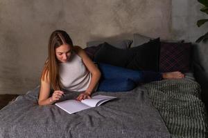 mujer acostada de lado en la cama y escribiendo notas en el cuaderno foto