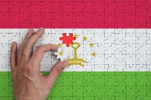 Tajikistan flag is depicted on a puzzle, which the man's hand completes to fold photo