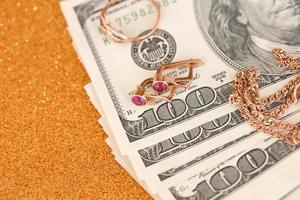 Expensive golden jewerly ring, earrings and necklace with big amount of US dollar bills on luxury glitter golden background surface. Pawnshop or jewerly shop photo