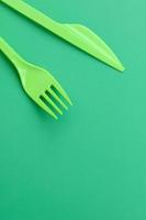 Disposable plastic cutlery green. Plastic fork and knife lie on a green background surface photo