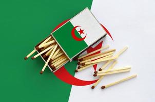 Algeria flag is shown on an open matchbox, from which several matches fall and lies on a large flag photo