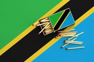 Tanzania flag is shown on an open matchbox, from which several matches fall and lies on a large flag photo