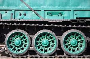 Side view of the vehicle on a caterpillar track with black tracks and green wheels and a side metal wall photo