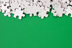 A pile of uncombed elements of a white jigsaw puzzle lies on the background of a green surface. Texture photo with copy space for text