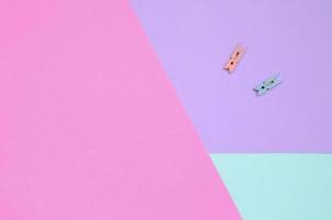 Two colored wooden pegs lie on texture background of fashion pastel violet, blue and pink colors paper in minimal concept photo