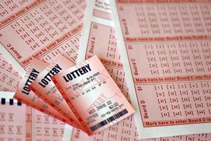 Red lottery ticket lies on pink gambling sheets with numbers for marking to play lottery. Lottery playing concept or gambling addiction. Close up photo