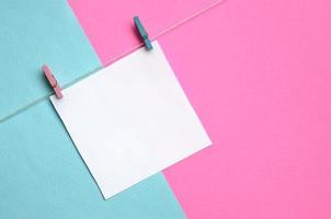 un trozo de papel cuelga de una cuerda con clavijas sobre fondo de textura de papel de colores azul pastel y rosa de moda en un concepto mínimo foto