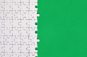 Fragment of a folded white jigsaw puzzle on the background of a green plastic surface. Texture photo with copy space for text