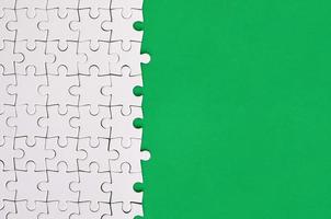 Fragment of a folded white jigsaw puzzle on the background of a green plastic surface. Texture photo with copy space for text