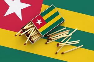 Togo flag is shown on an open matchbox, from which several matches fall and lies on a large flag photo